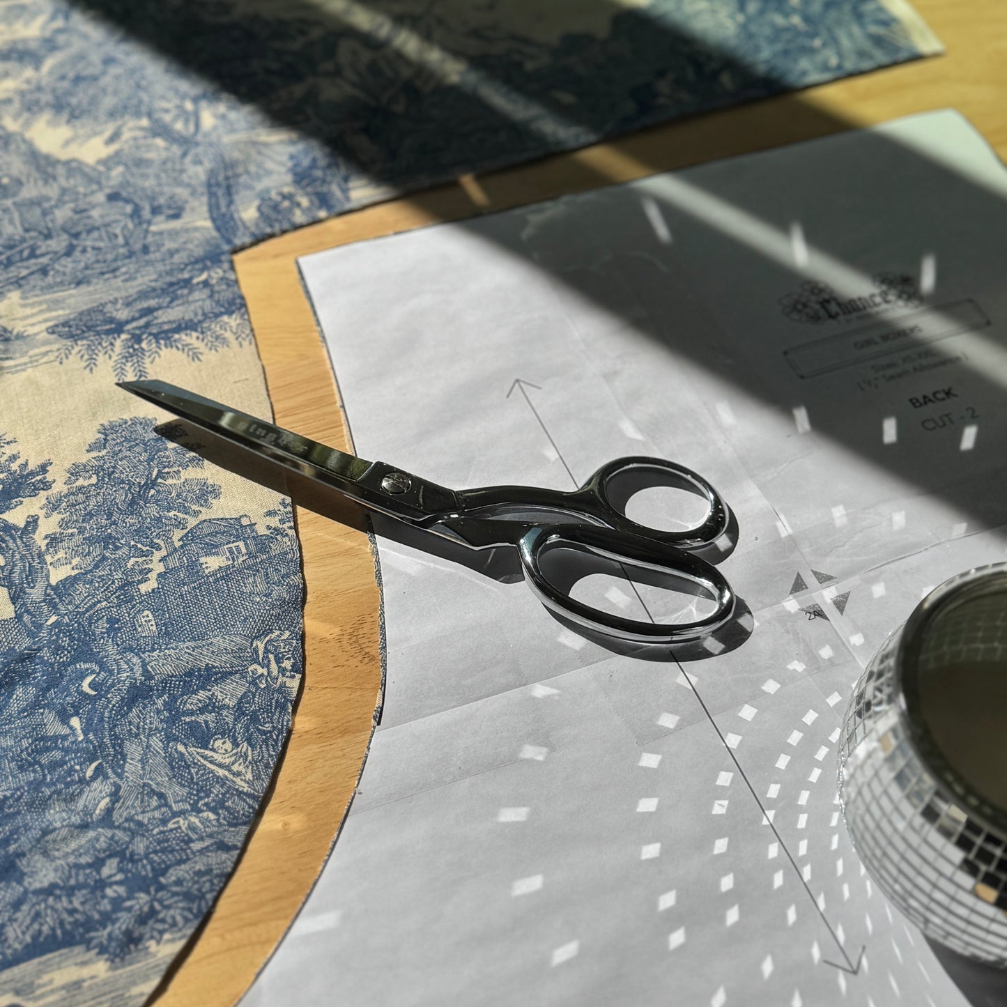 Scissors on a piece of fabric with a patterned tablecloth in the background
