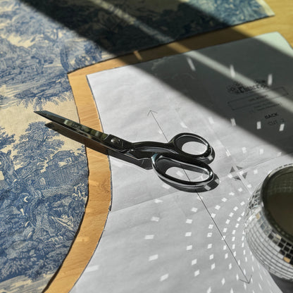 Scissors on a piece of fabric with a patterned tablecloth in the background
