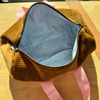 A mustard yellow corduroy zippered pouch or small bag with pink handles, shown open on a wooden table with a ruler nearby.